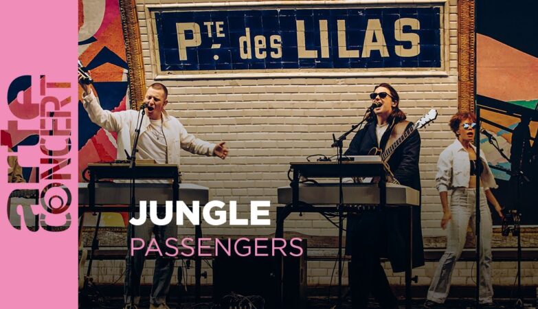Live band performing on an outdoor stage with two keyboardists and a guitarist; poster reads Jungle Passengers.